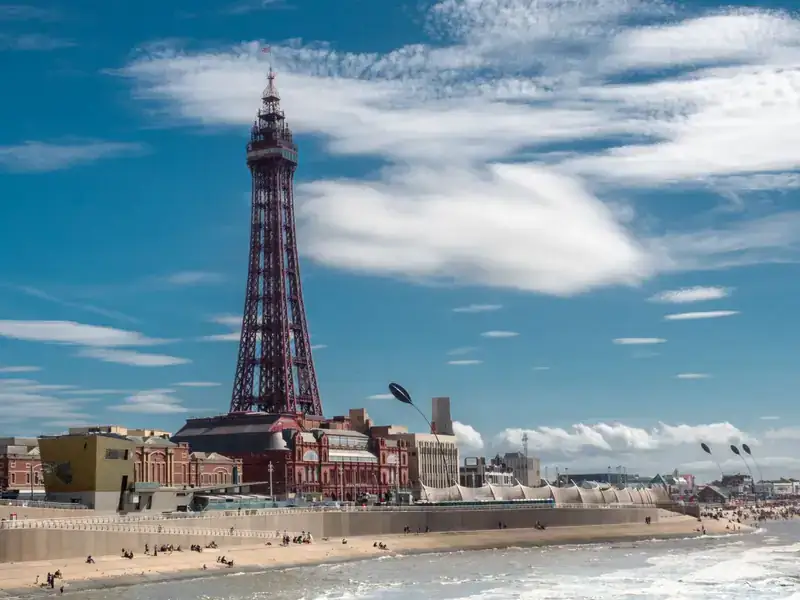 Blackpool Tower rising above the seafront and beach under a blue sky with white clouds