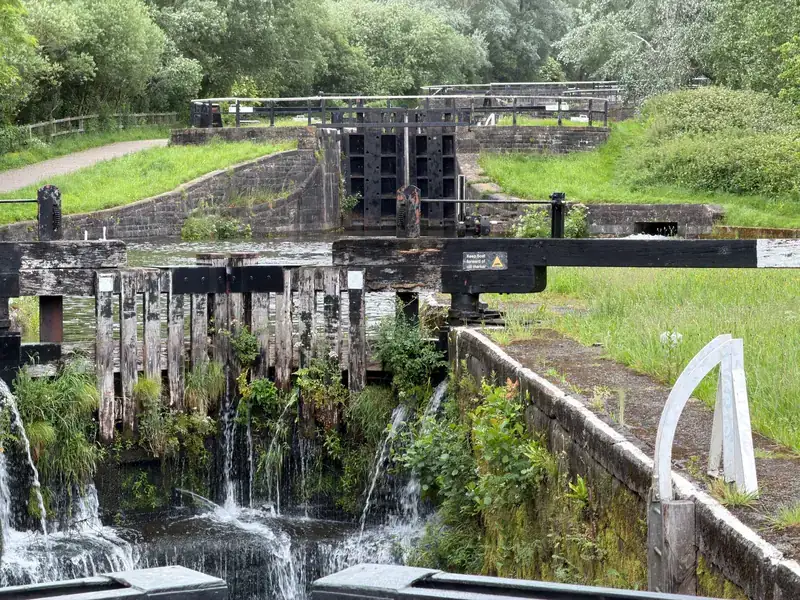 A lock on the Leeds and Liverpool Canal in Wigan, with water spilling through the wooden gates and green banks beyond