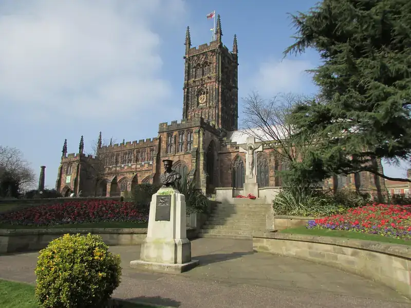 St Peter's Collegiate Church in Wolverhampton behind flower beds and a memorial on a sunny day