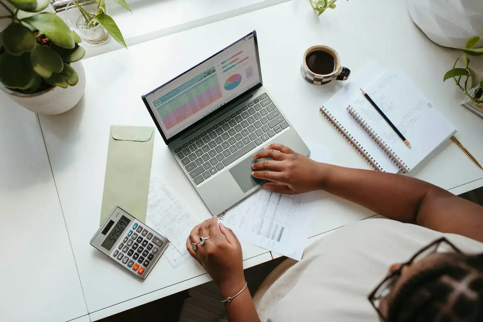 Overhead view of someone using a budget spreadsheet on a laptop beside a calculator and notebook