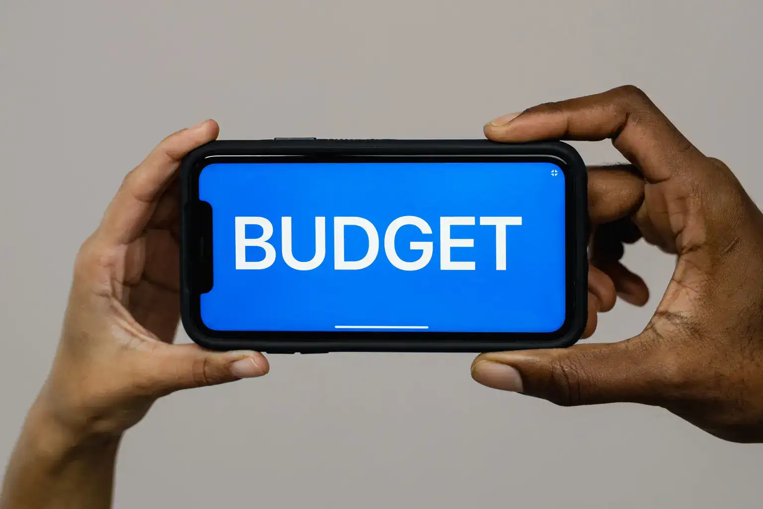 Two hands hold a smartphone sideways with the word budget shown on its screen