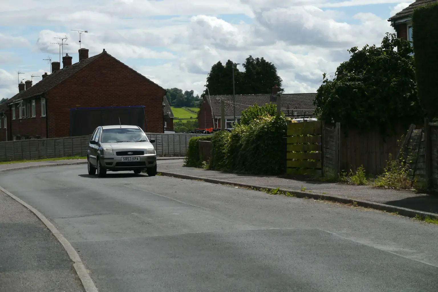 A silver hatchback driving along a curving road through a British housing estate