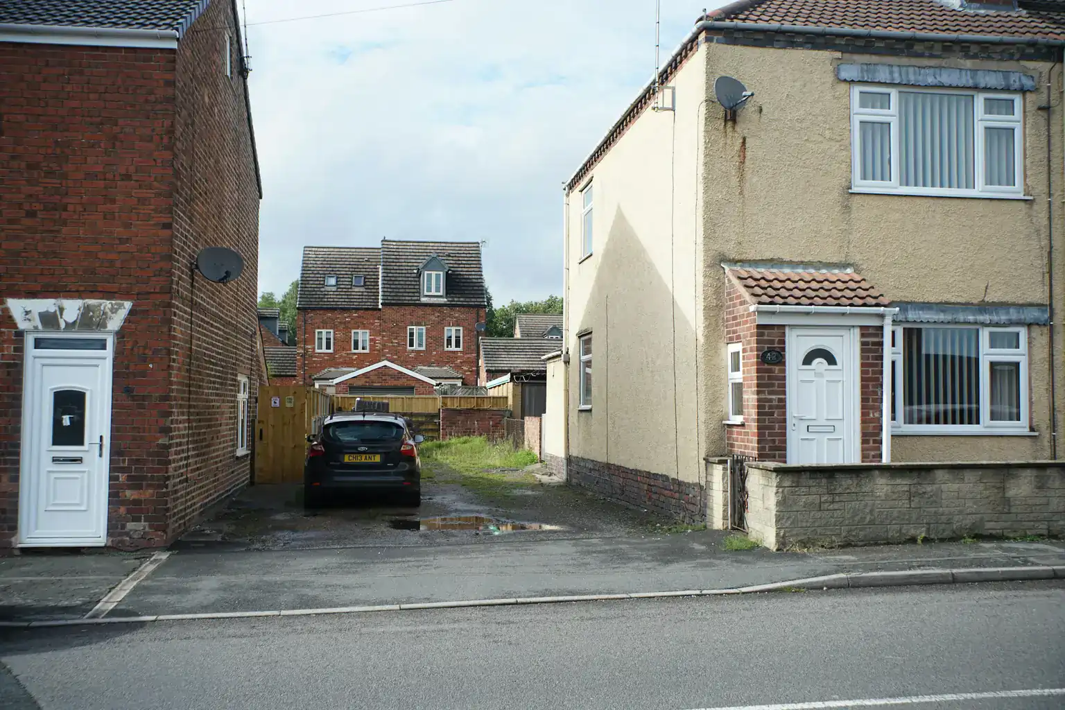 A black car parked on a shared driveway between two brick semi-detached houses