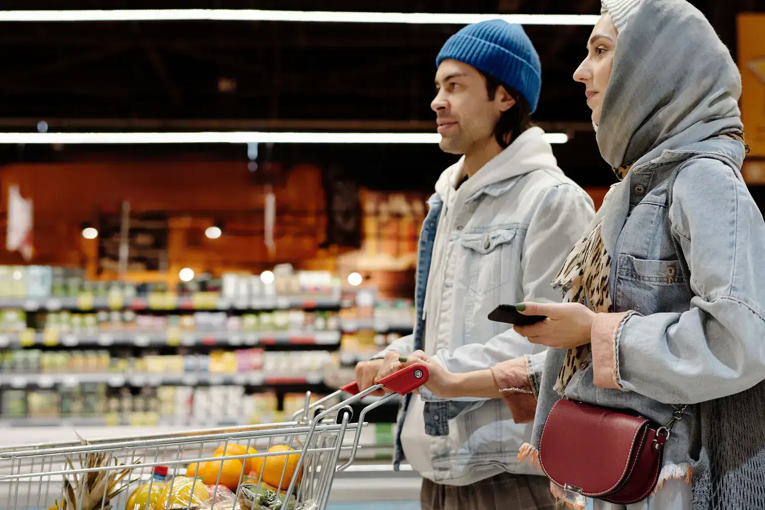 A young couple pushing a supermarket trolley with fruit past shelves of groceries