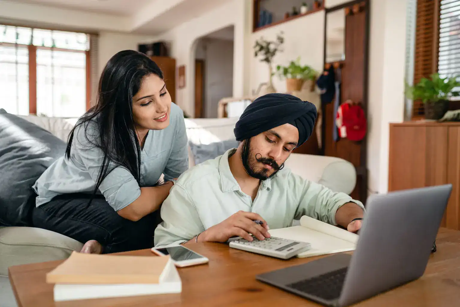 A couple at home work through their finances with a calculator, notebook and laptop