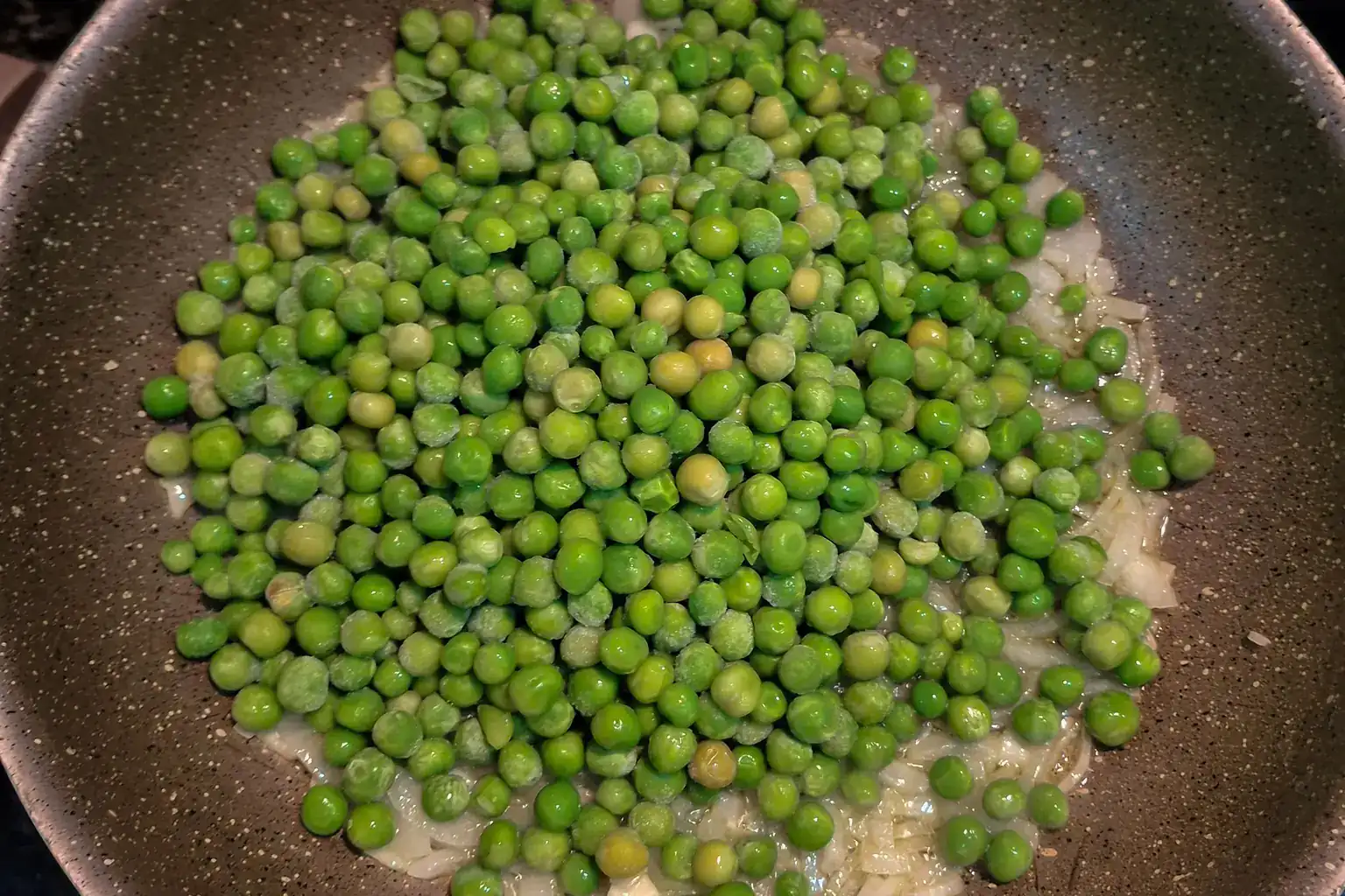 Frozen garden peas cooking with chopped onion in a non-stick frying pan
