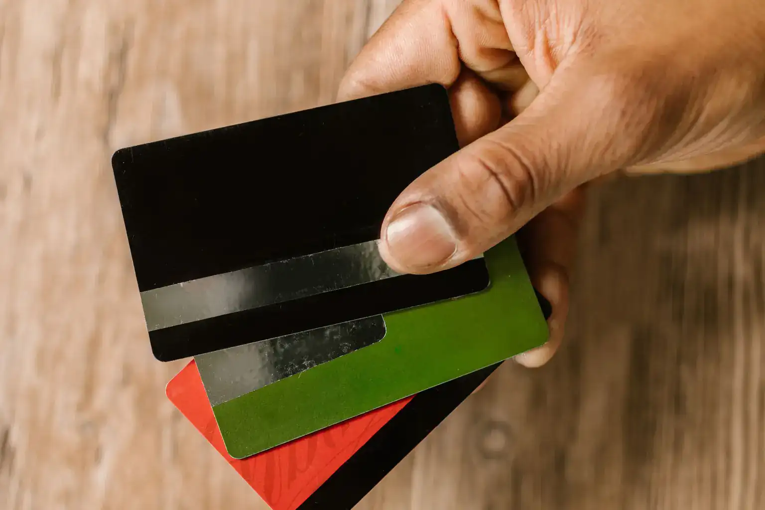 A hand holding three plain credit cards fanned out above a wooden table
