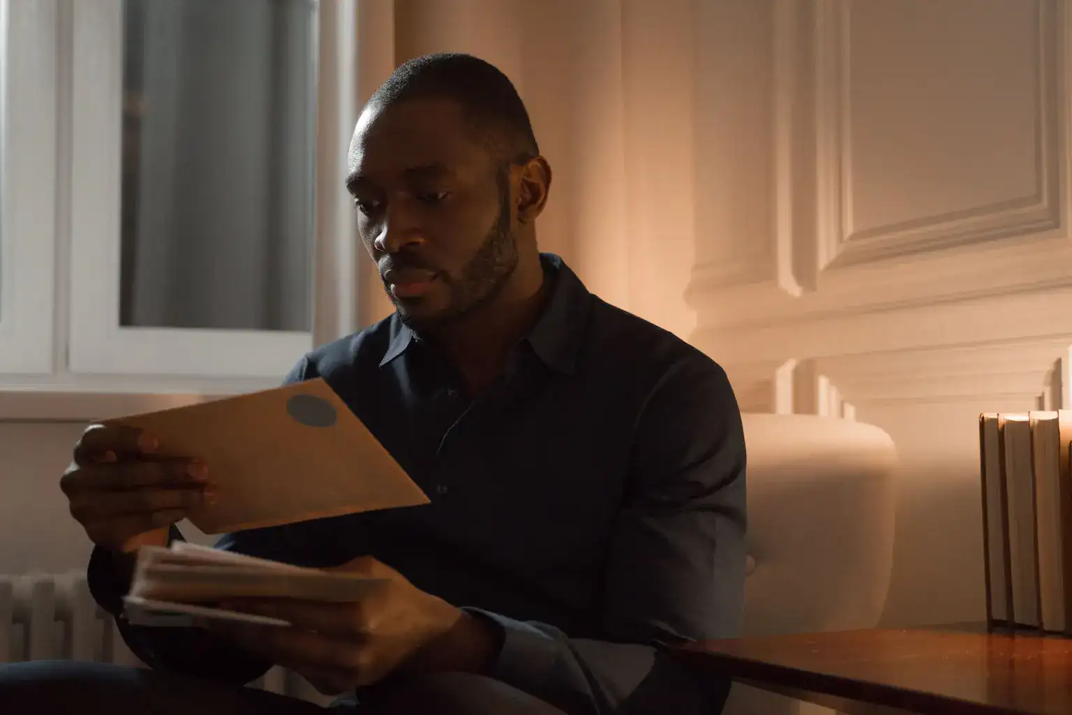 A man sitting in an armchair at home opens and reads through a pile of envelopes