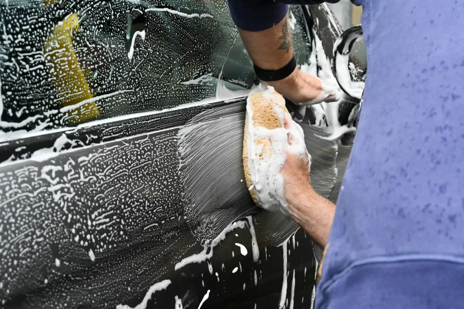 A man scrubbing the soapy door of his dark car with a sponge