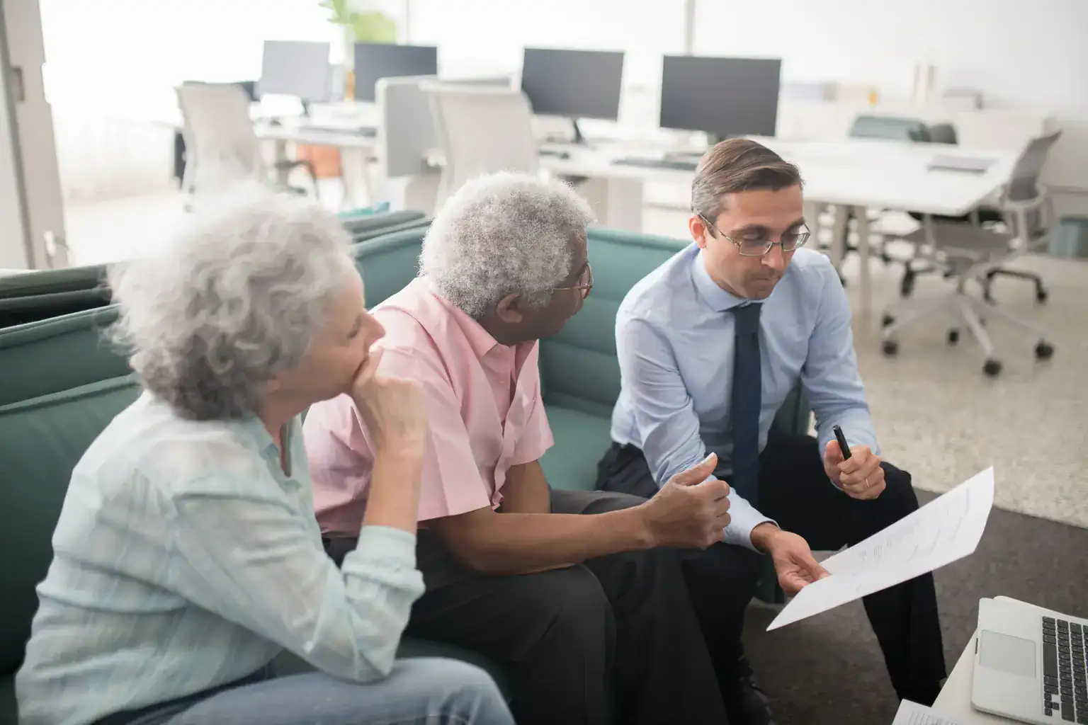 An older couple sit on a sofa reviewing paperwork with an adviser in an office