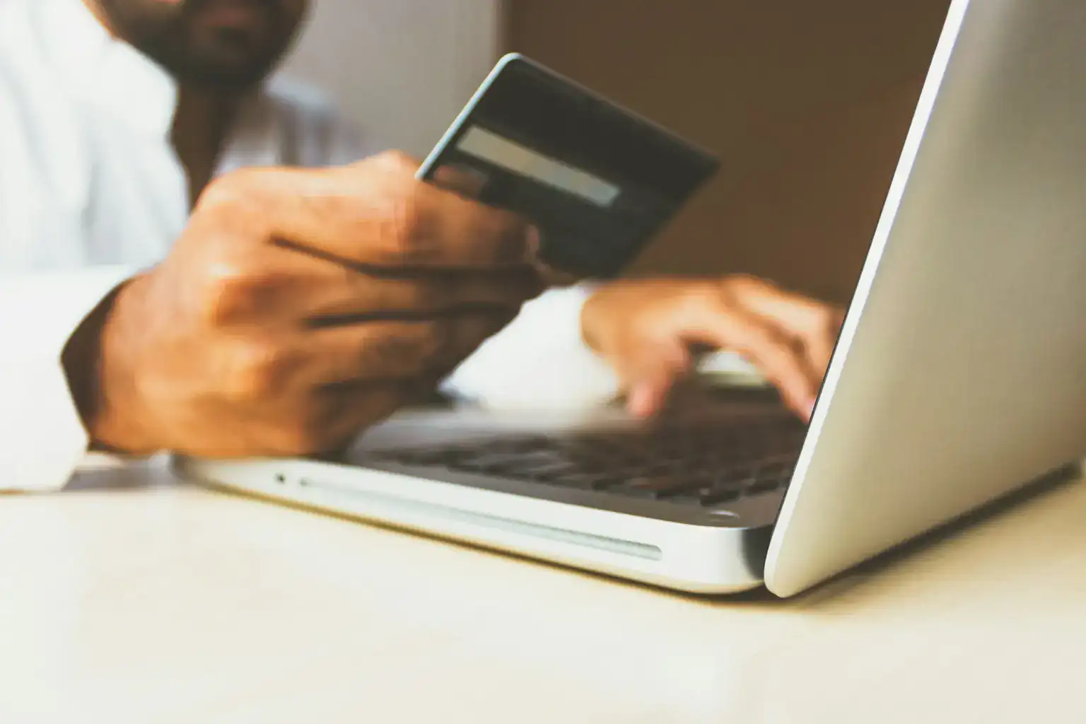 A person holds a payment card while typing on a laptop to pay online