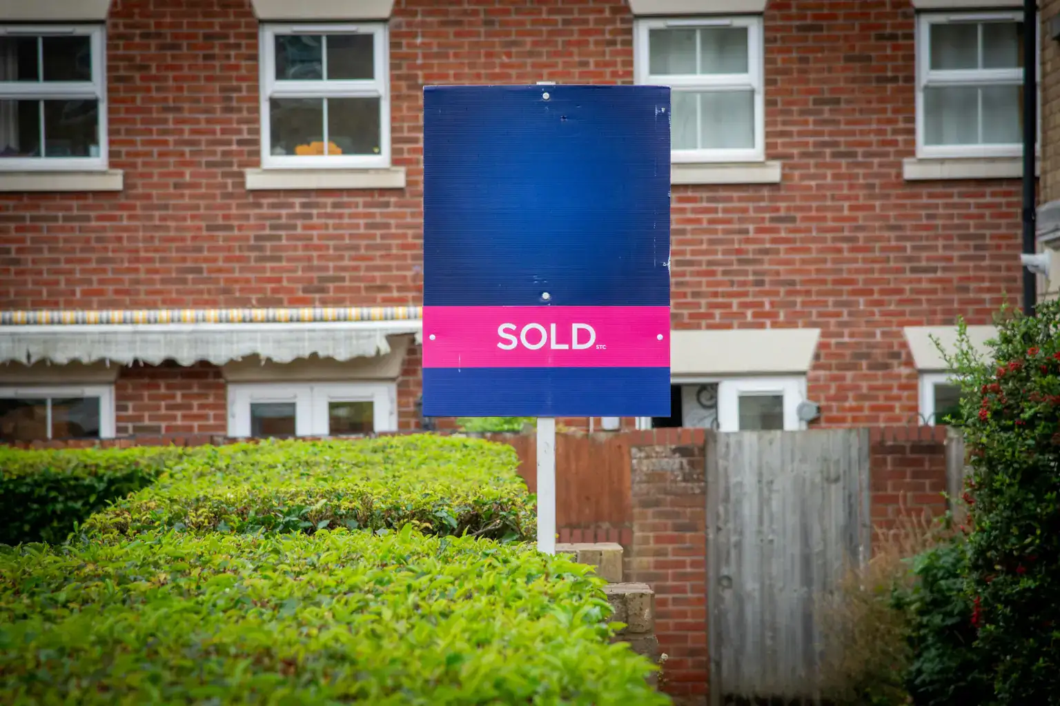 A sold sign standing behind a neat hedge in front of a modern brick house
