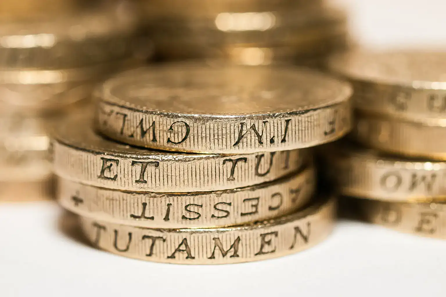 Close-up of stacked British one pound coins showing the edge inscription