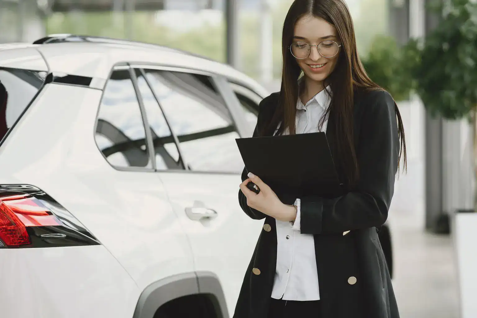 A smiling woman holds a document folder while standing beside a white car